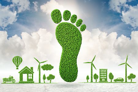 grüner Fußabdruck, dazu Windräder, Bäume Häuser, Auto, Motorrad, Heißluftballon (alles aus Gras)