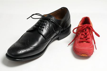 Links ein schwarzer Herrenschuh, rechts ein roter Kinderturnschuh