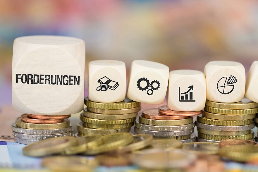 Verschiedene W&uuml;rfel stehen auf M&uuml;nzgeld, auf einem W&uuml;rfel steht "Forderungen"