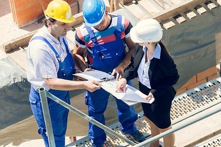 drei Personen &uuml;ber einen Plan gebeugt auf der Baustelle im Gespr&auml;ch